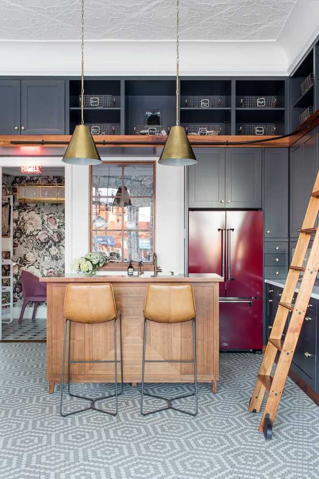 Studio kitchenette with a butcher-block island, leather stools, a red refrigerator and charcoal cabinetry above