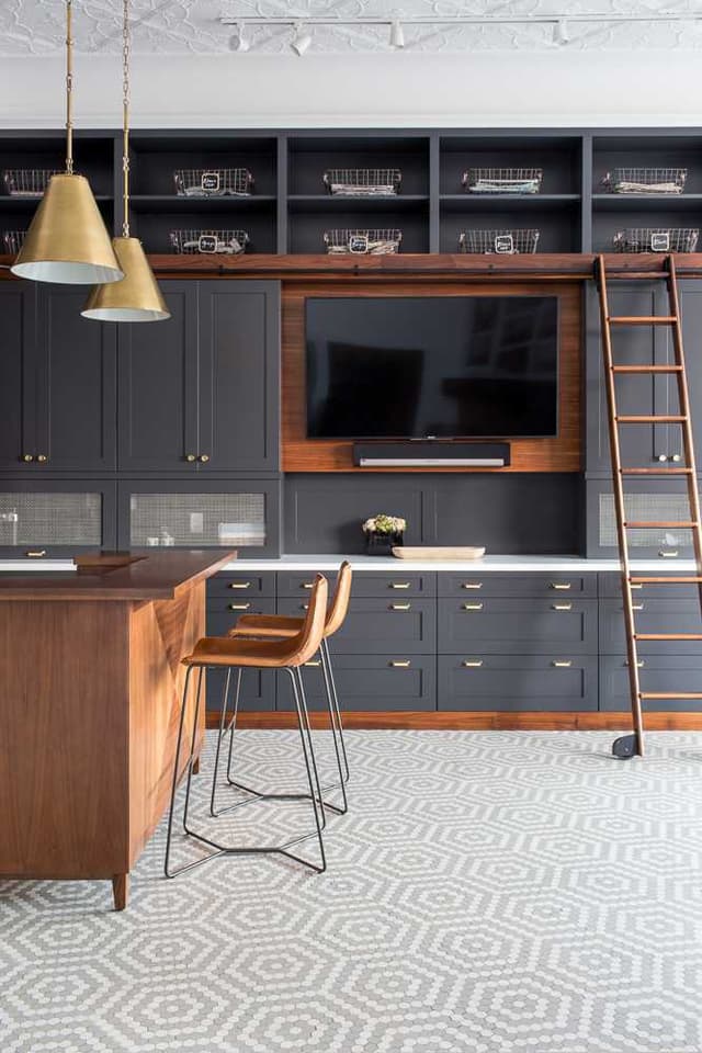 Built-in charcoal cabinetry with open shelving, a rolling library ladder and a walnut desk