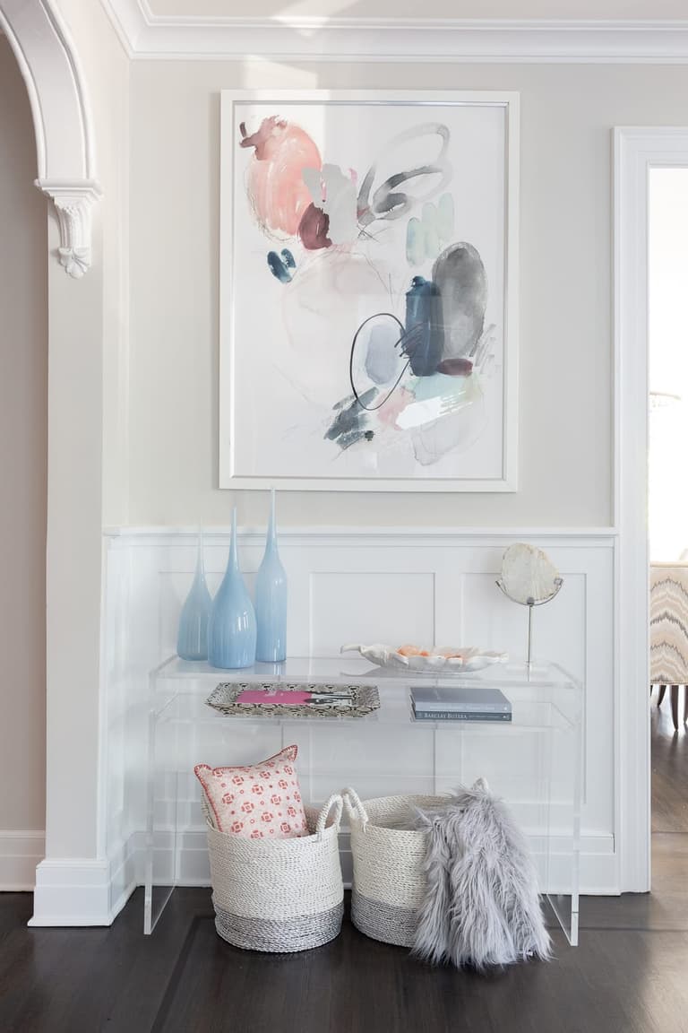 Hall beneath an arched opening, with an acrylic console table, framed artwork and woven storage baskets below