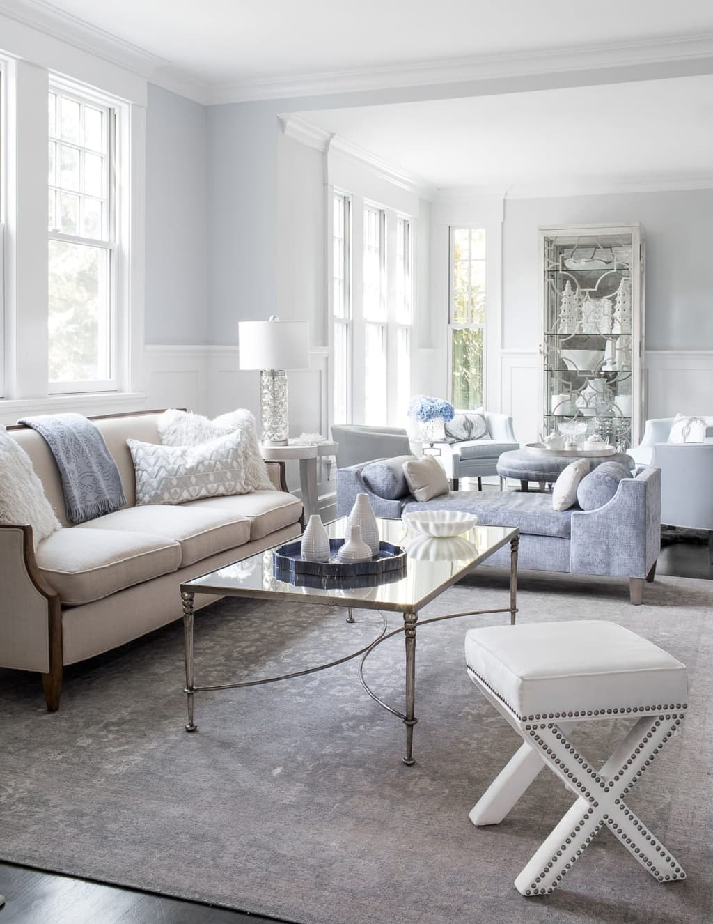 Living room with paneled wainscot, a tufted sofa, a mirrored coffee table and an X-bench by the window
