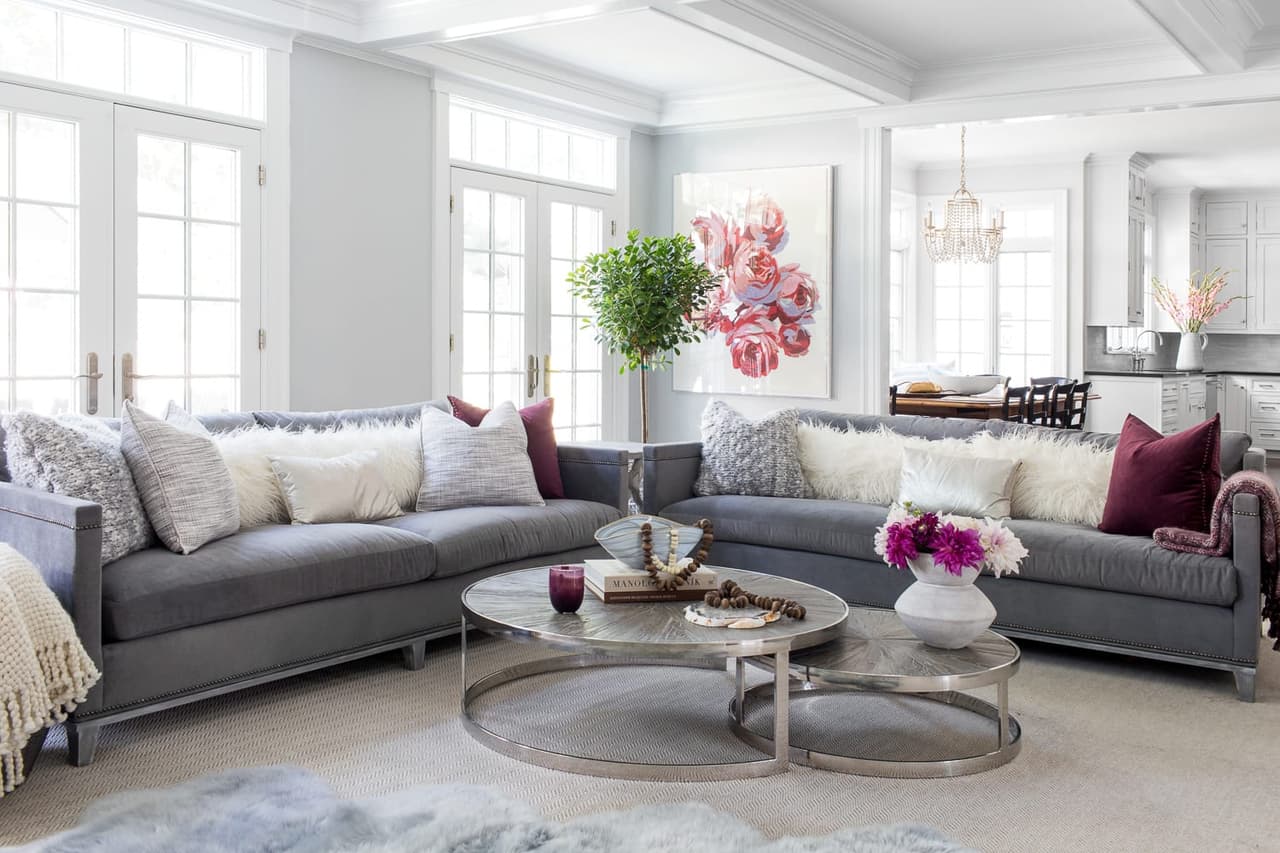 Family room with a curved gray sectional, round nesting coffee tables and French doors opening to the terrace