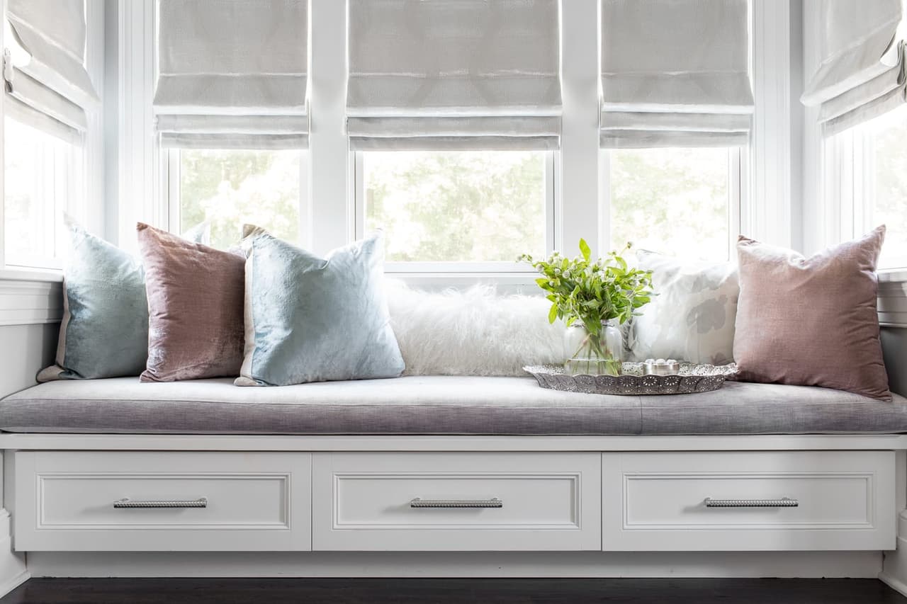 Window seat with drawer storage below, cushioned seating and woven Roman shades across three windows