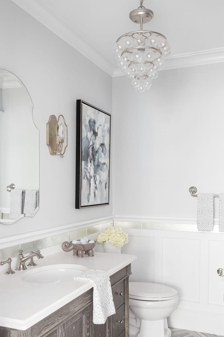 Bathroom with a gray vanity, an oval mirror, board wainscot and a glass pendant overhead