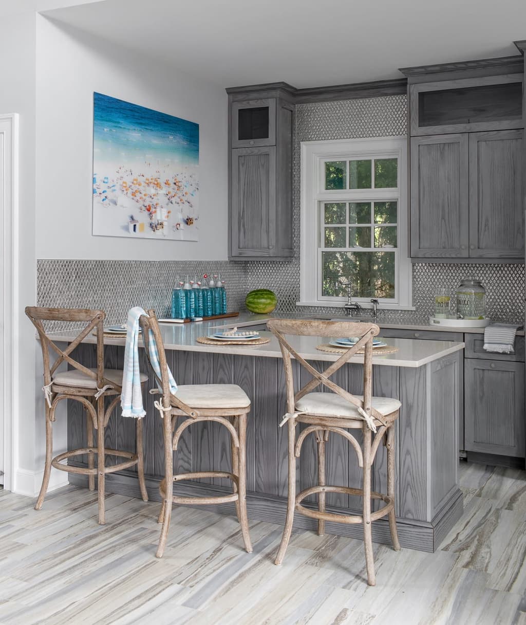 Pool house kitchenette with weathered gray cabinetry, a counter-height island and rush-seat stools