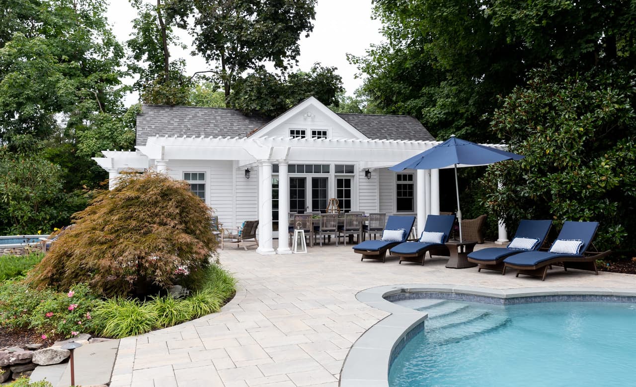 Pool and raised spa with a paver surround, navy loungers and the columned pool house beyond