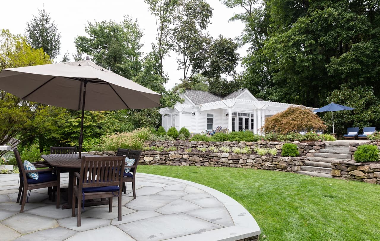 Bluestone dining terrace with an umbrella table and chairs, looking back toward the pool house
