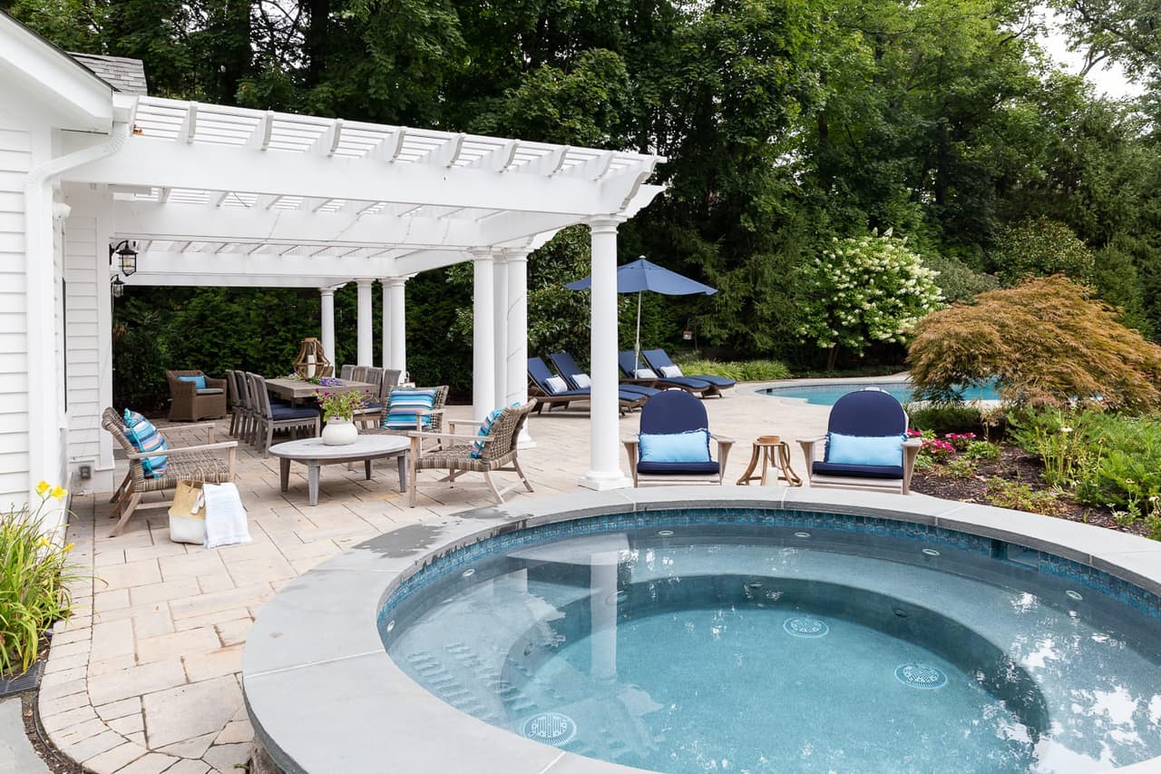 Pergola and lounge seating beside the pool and spa of a Short Hills, NJ home, built by Michael Robert Construction