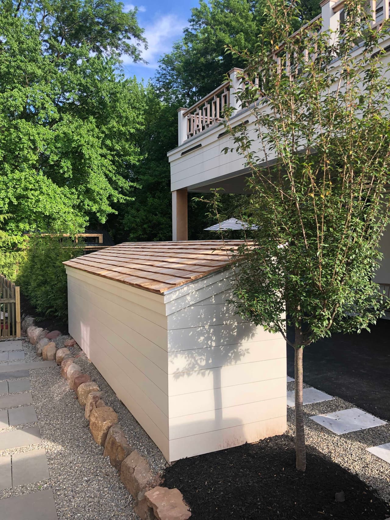 Screened store for bins and bicycles built in cedar beside the drive of a Westfield, NJ home, with a slatted lid and a tree planted alongside