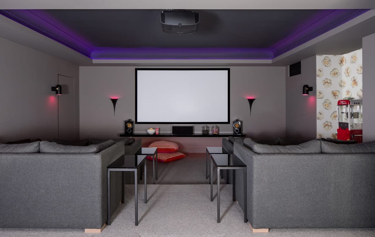 Home theater in the Mroz family home in Westfield, NJ, with two sectionals facing the screen and a purple cove light around the ceiling