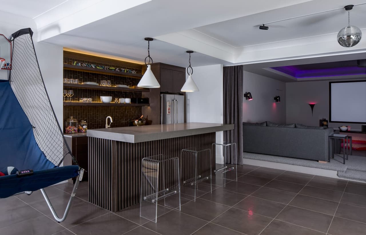 Lower level of the Mroz family home in Westfield, NJ, with a corrugated bar front, acrylic stools, an arcade basketball game and the theater beyond