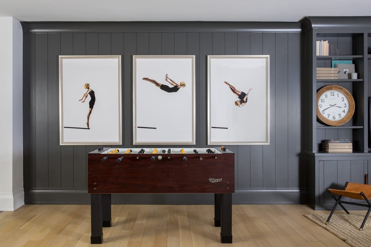 Basement game room with a charcoal paneled wall, three framed diving photographs and a foosball table