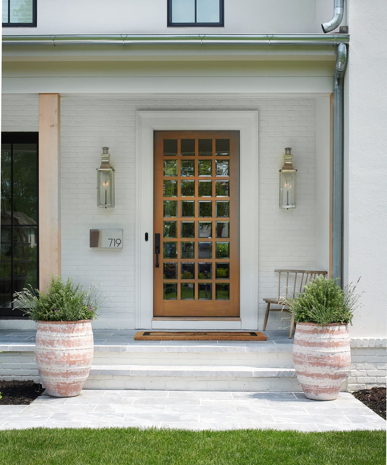 Glazed wood front door and sconces on the white painted brick of the Mroz family home in Westfield, NJ, with planted urns on the step