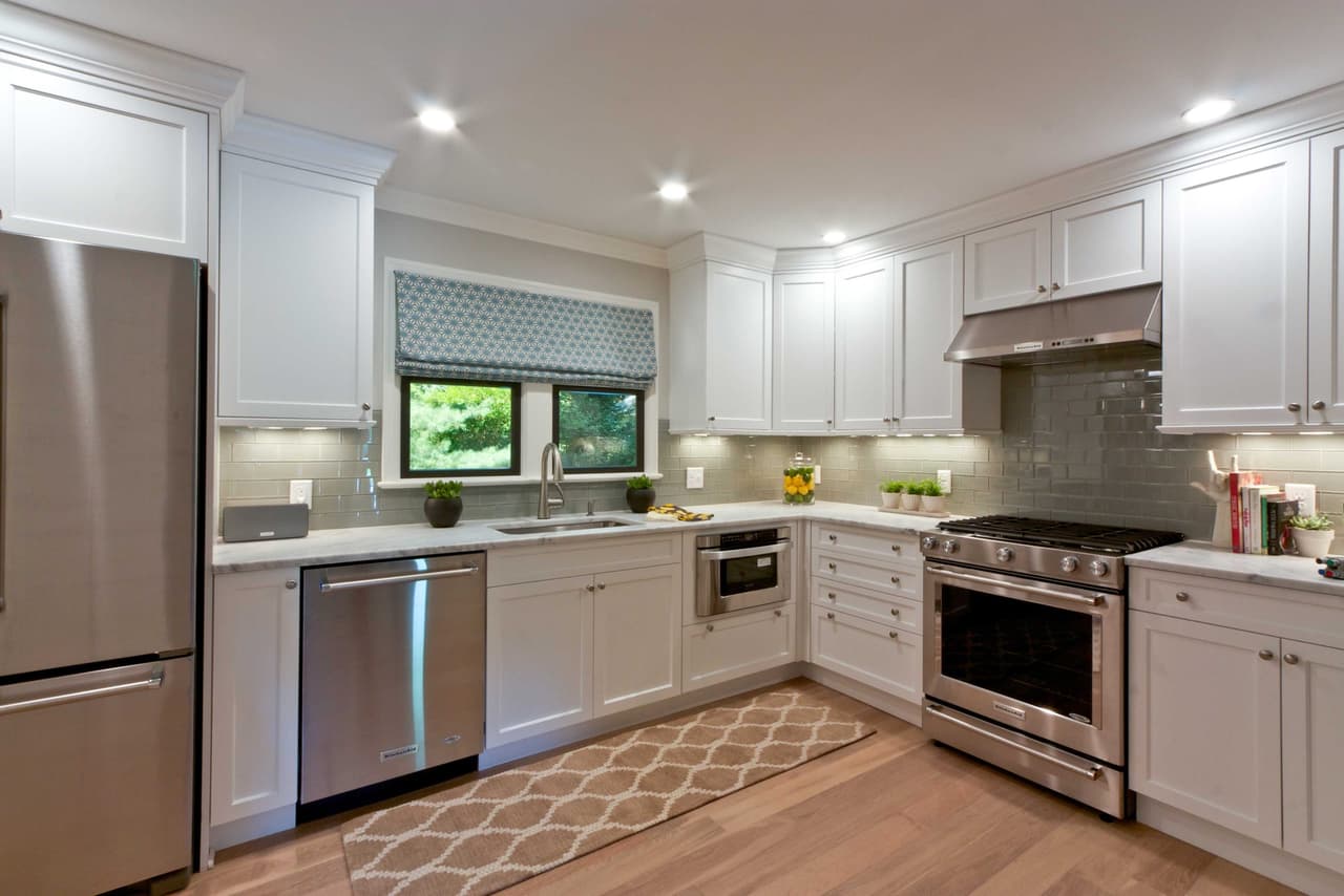Kitchen with white cabinetry, stainless appliances, a patterned roman shade and a runner on oak floors