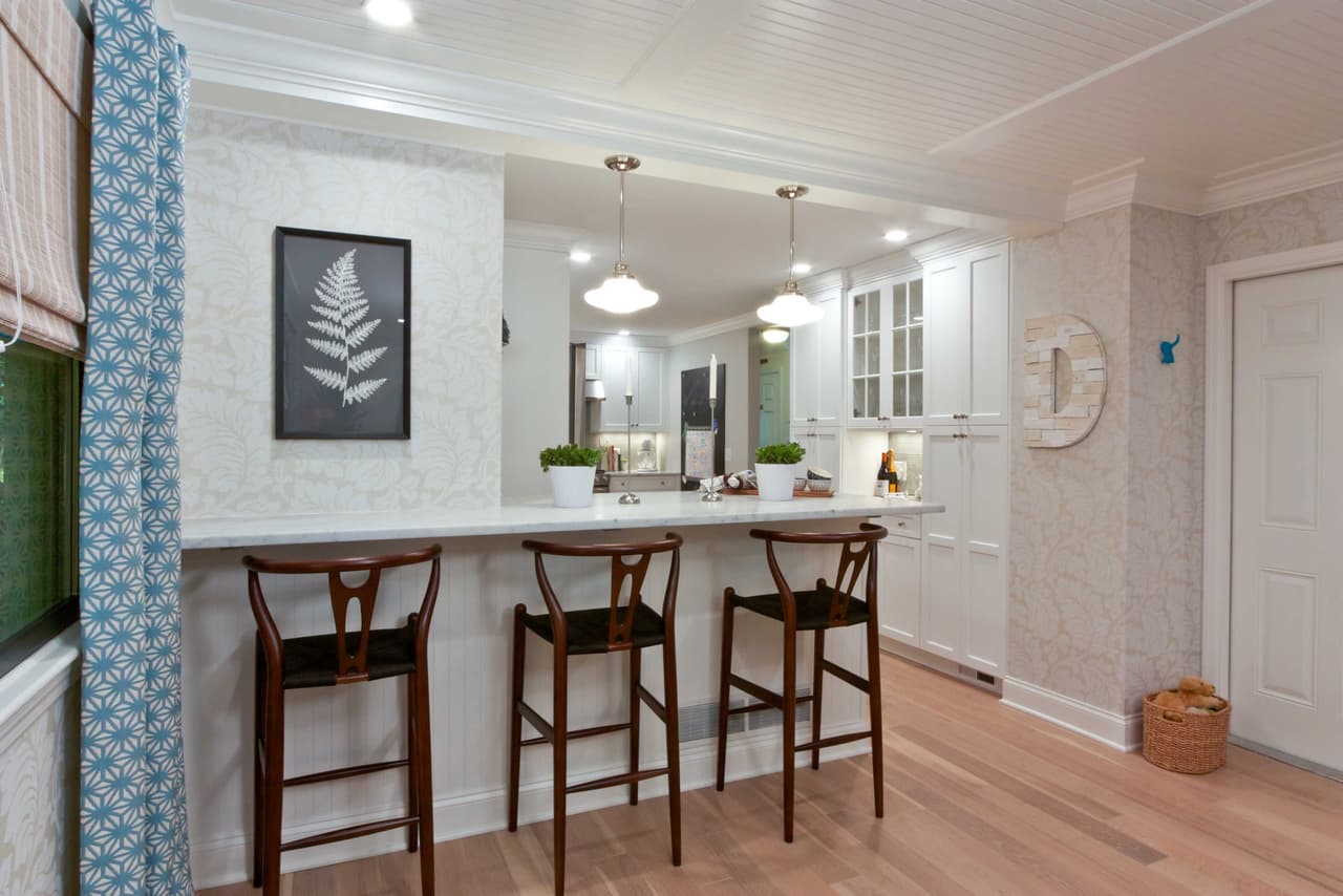 Opened-up kitchen seen from the living room, with a peninsula, three bentwood stools and pendant lights
