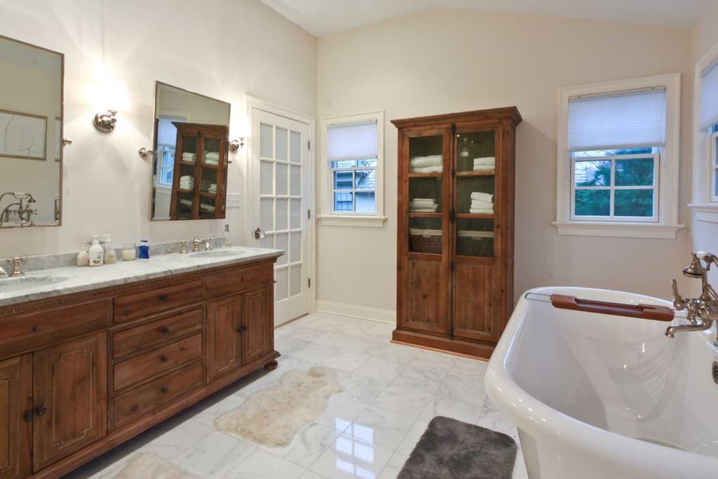 Bathroom with a marble floor, a wood-paneled door, a vanity with a framed mirror and a tub beyond