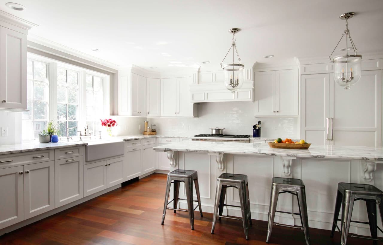 Kitchen with white cabinetry, a farmhouse sink under the window, lantern pendants and dark wood floors