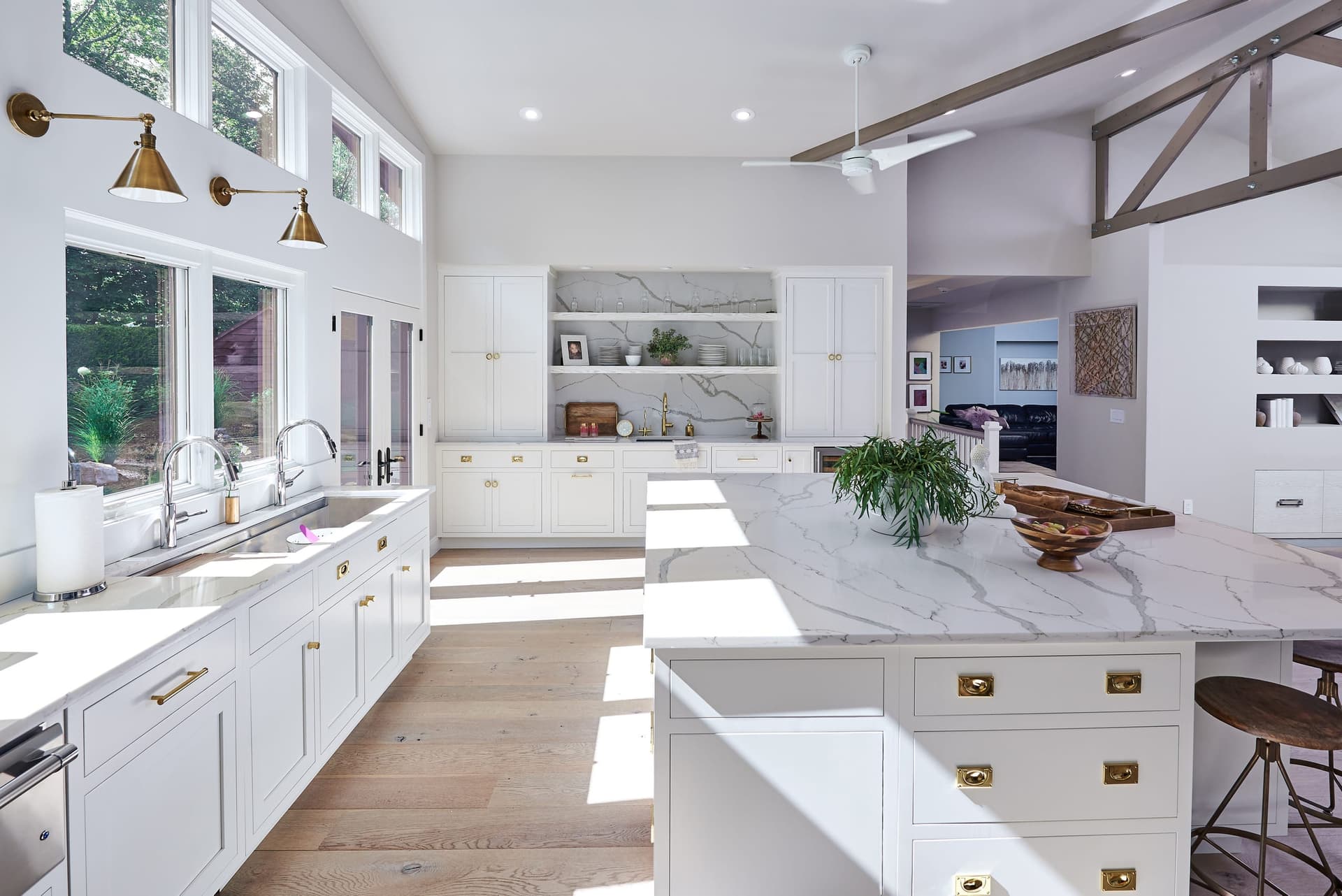Kitchen of a Scotch Plains, NJ farmhouse renovation, with a marble waterfall island, brass pendants, open shelving and an exposed truss over the range wall