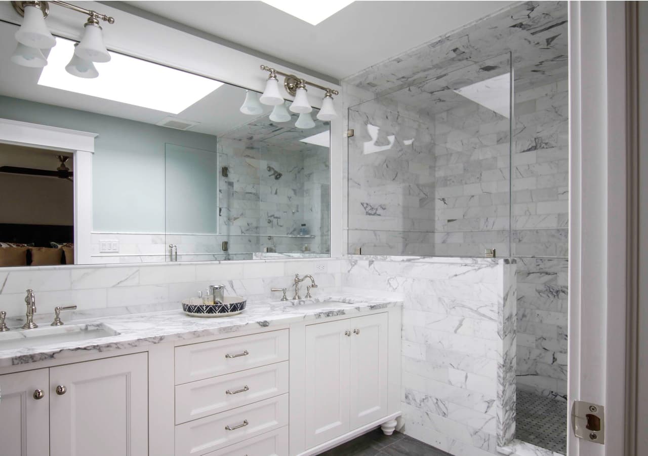 Primary bathroom vanity in marble with a wall of mirror, under a skylight and track lighting