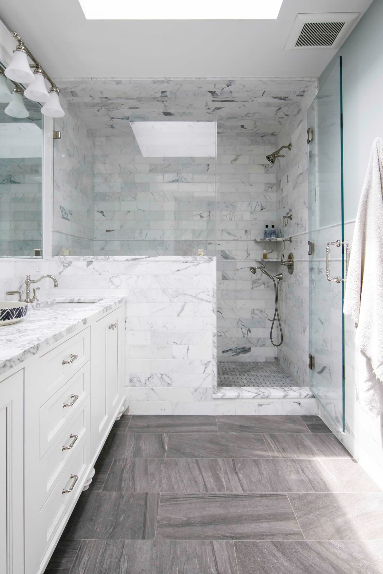 Primary bathroom with a marble-tiled walk-in shower, a long vanity and a herringbone stone floor