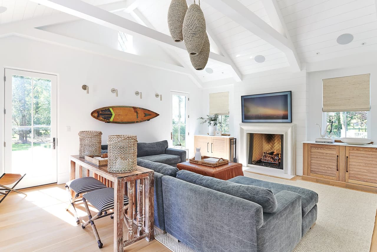 Family room of the Mroz family home in Westfield, NJ, under a vaulted plank ceiling, with a surfboard against the wall and a fireplace between built-ins