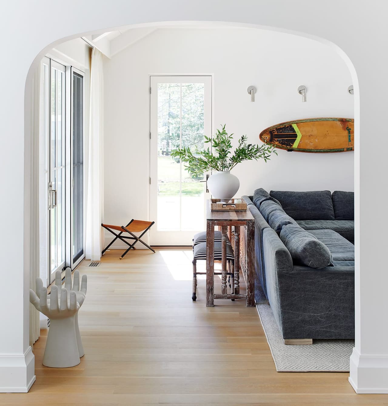 Mudroom and rear hall under an arched opening, with wall hooks, a surfboard overhead and a navy sectional beyond