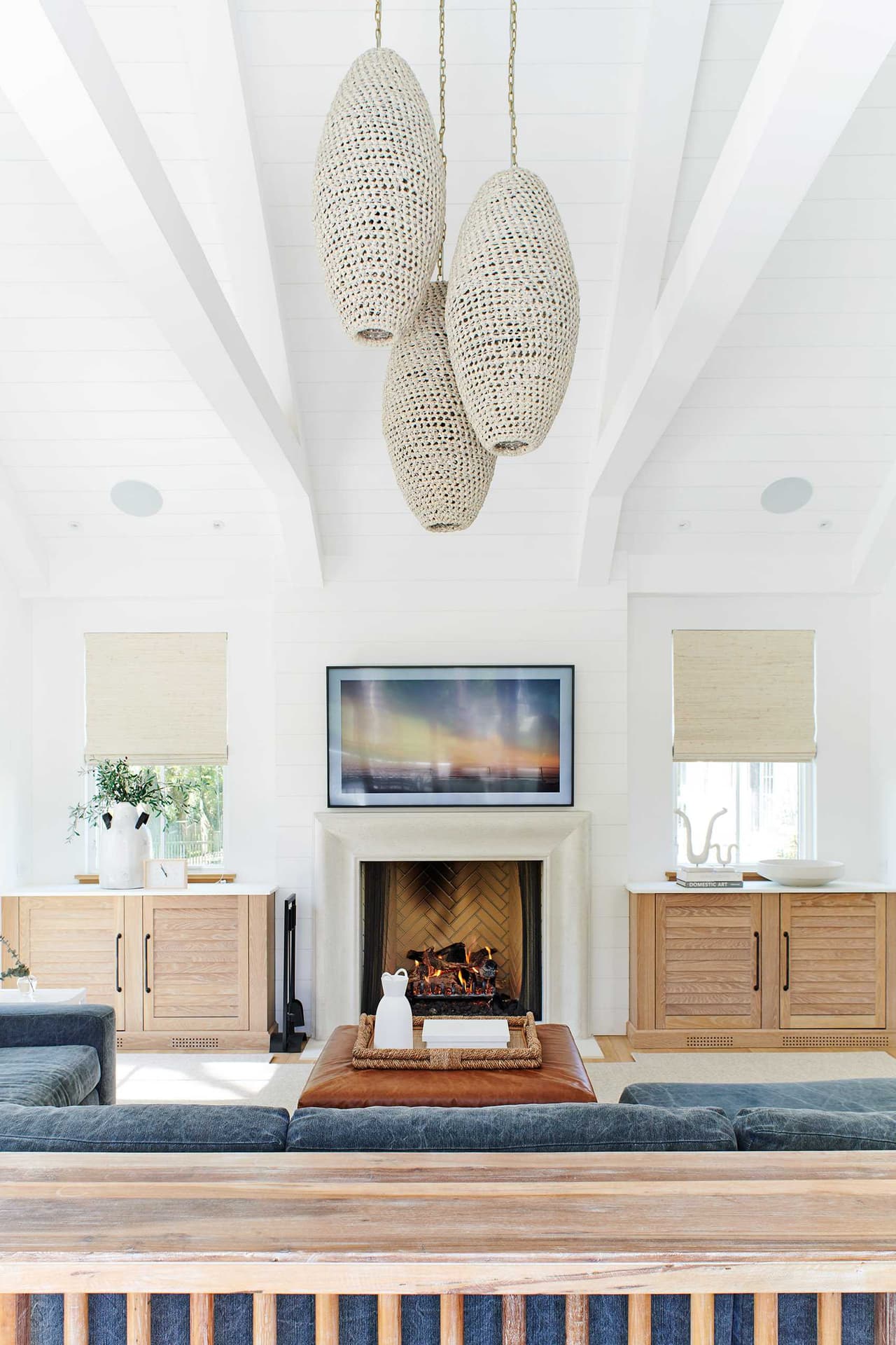 Lounge under a vaulted white ceiling with painted beams, three woven pendants and a fireplace between built-in cabinets