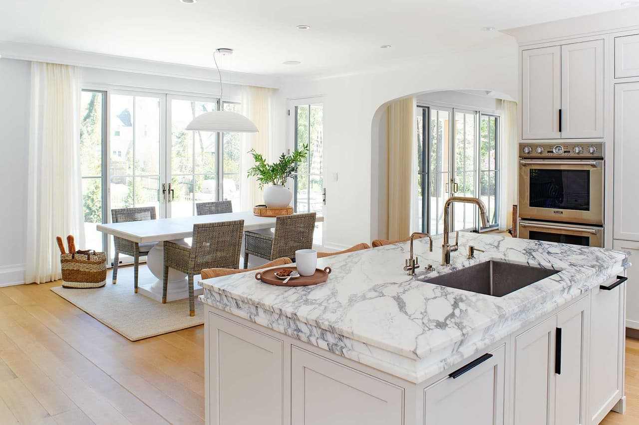 Kitchen island topped in book-matched marble with an undermount sink, open to the dining area and a wall of windows
