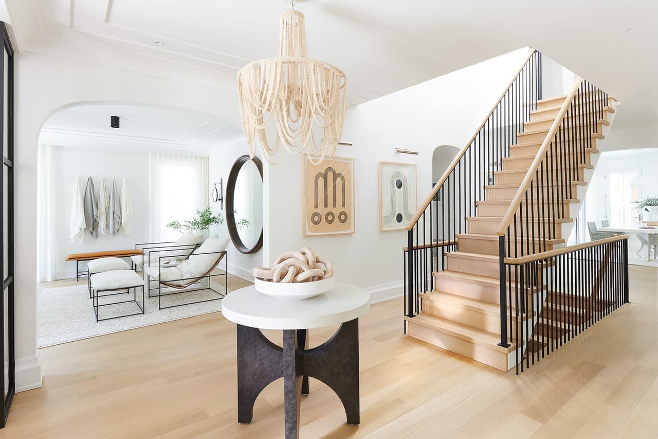 Hall of the Mroz family home in Westfield, NJ, looking past a round mirror and a stone pedestal table to the oak stair with black balusters