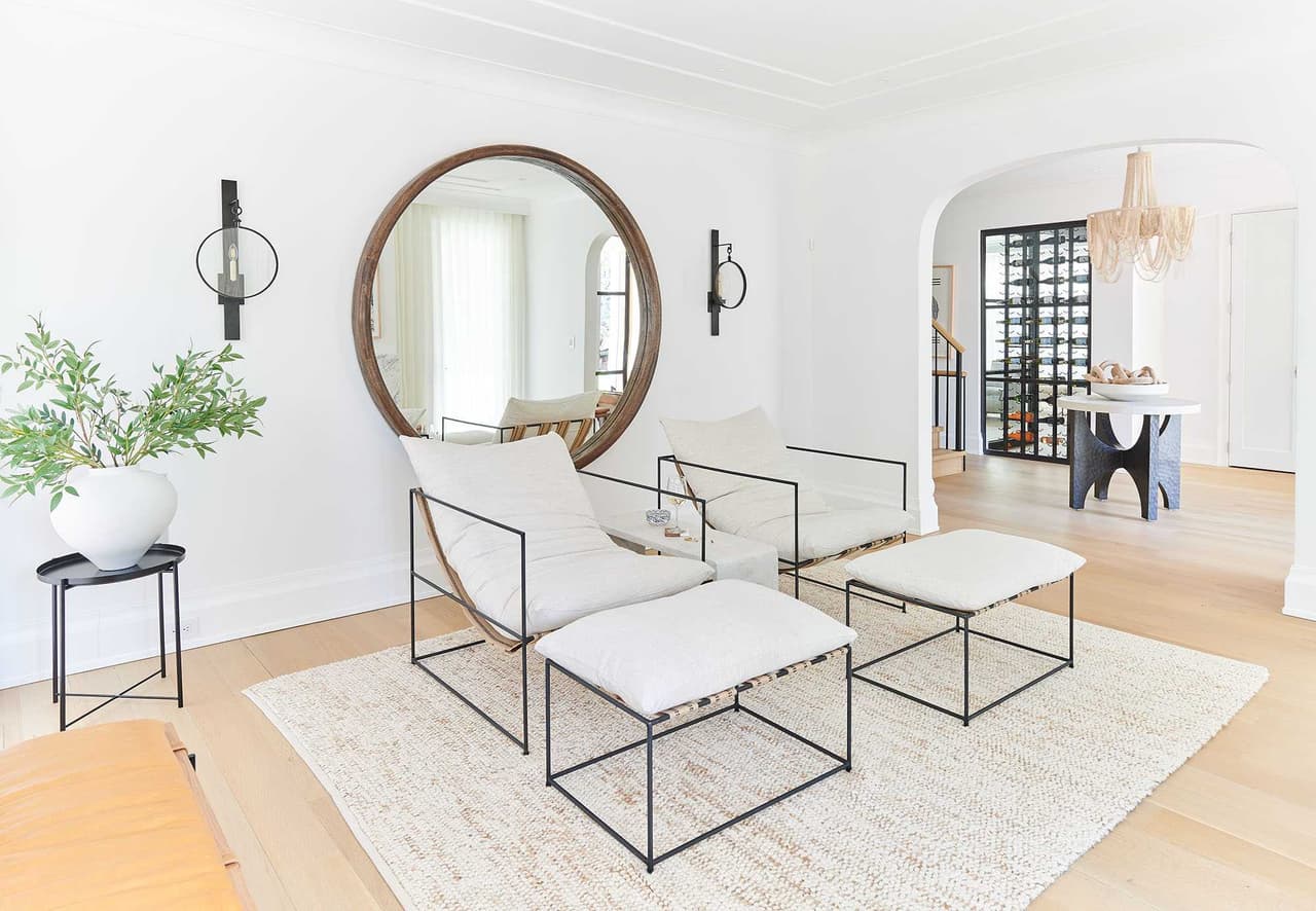 Living room with a large round mirror over a plaster fireplace, paired benches and a pale wool rug