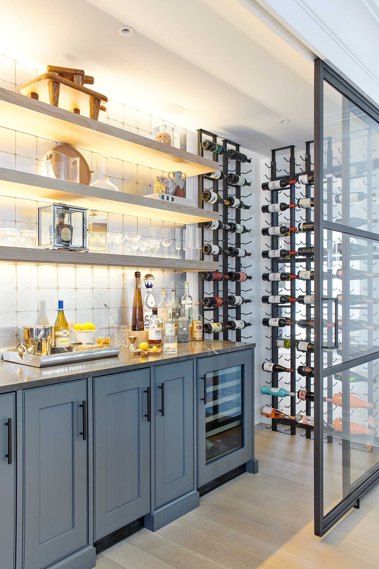 Bar with blue-gray cabinetry, lit open shelving and a steel-and-glass wine wall