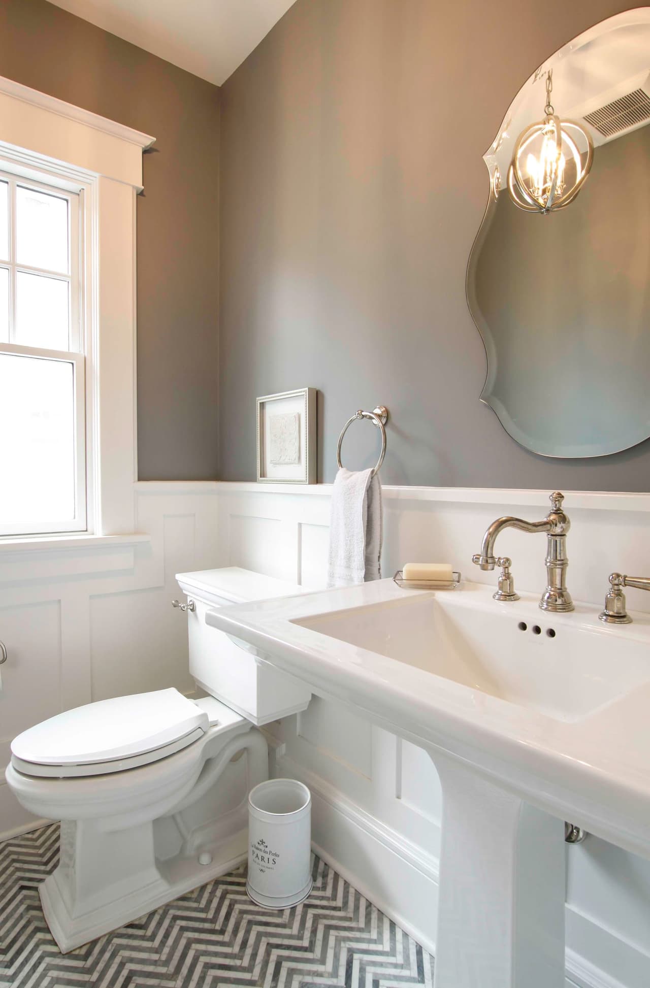 Powder room with a pedestal sink, an oval mirror, board wainscot and a patterned tile floor