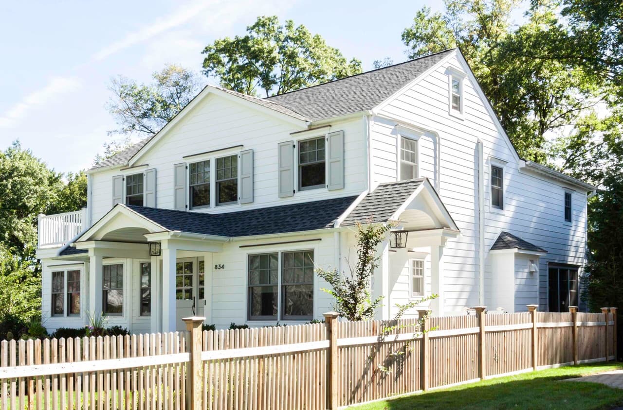 Side elevation of a white clapboard home with gabled dormers, dark window trim and a picket fence in Westfield, NJ