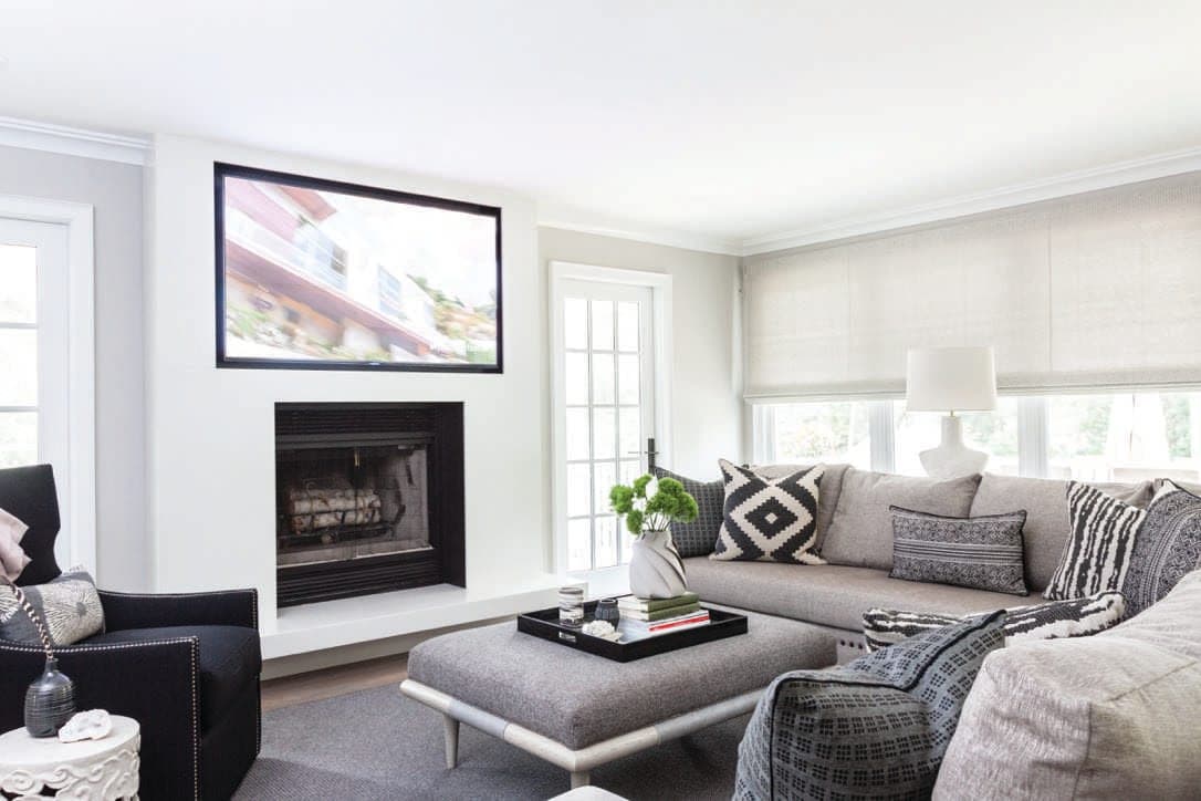 Family room with a sectional, an upholstered ottoman and a television above the fireplace