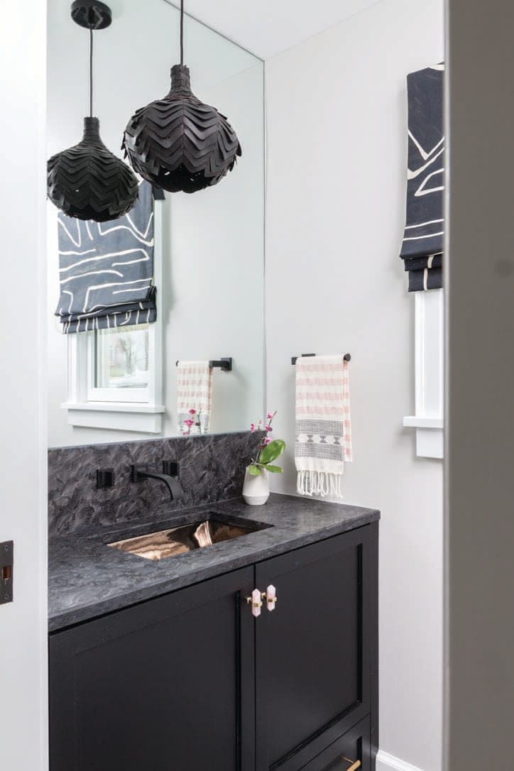 Powder room with navy cabinetry, a dark stone counter, scalloped black pendants and a wall mirror