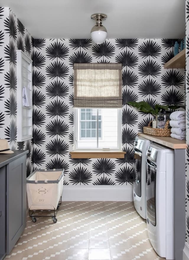 Laundry room papered in a black and white palm print in a Westfield, NJ home, with a wood counter over the machines and a canvas cart below the window