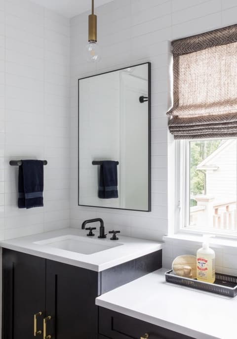 Bathroom in a Westfield, NJ home with a trough basin on a navy vanity, a black-framed mirror and a woven Roman shade at the window