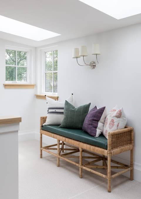 Rattan settee with green and pink cushions under a skylight and a pair of sconces in a Westfield, NJ home