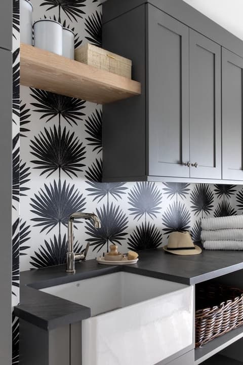 Laundry room in a Westfield, NJ home with a black and white palm-print wall, gray upper cabinets, a floating oak shelf and an apron sink