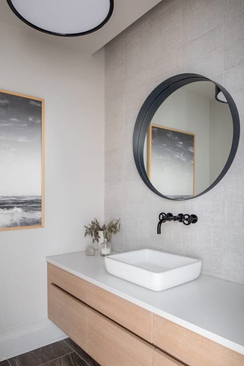 Vessel basin on a floating oak vanity under a round mirror and a framed seascape in a Westfield, NJ bathroom, with a black wall-mounted tap