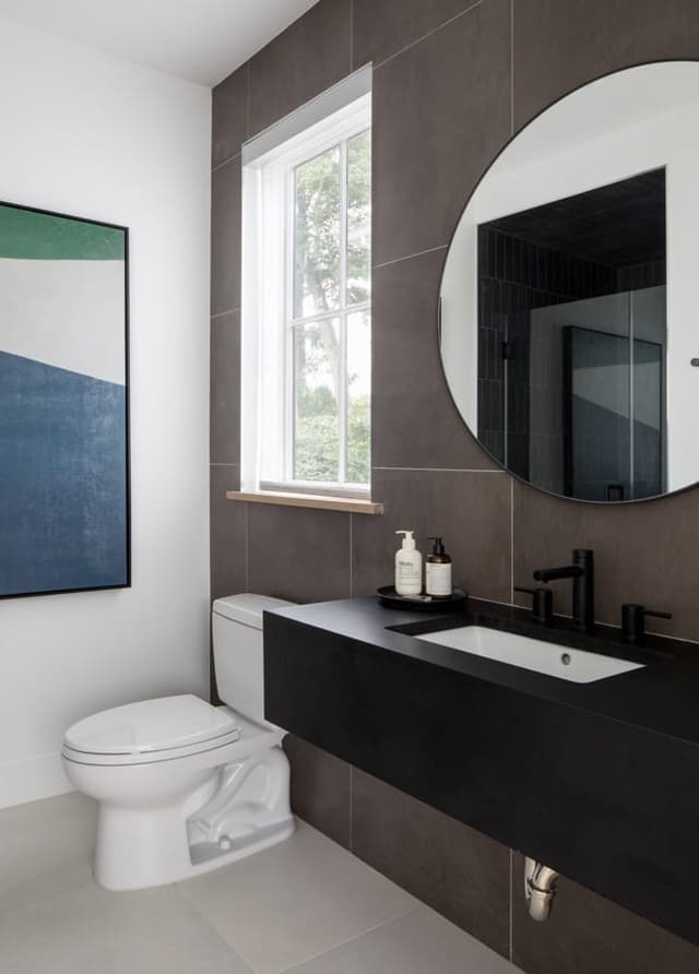 Bathroom in a Westfield, NJ home with a dark floating vanity, a round mirror on a charcoal tiled wall and a window alongside