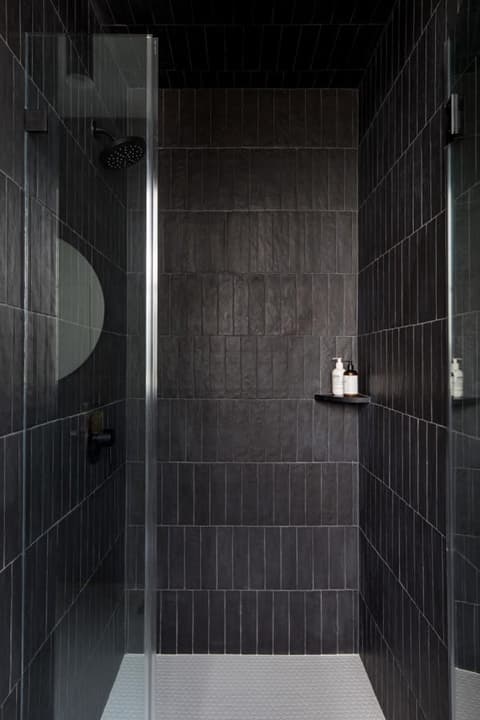 Shower lined floor to ceiling in charcoal stacked tile behind a glass door in a Westfield, NJ bathroom