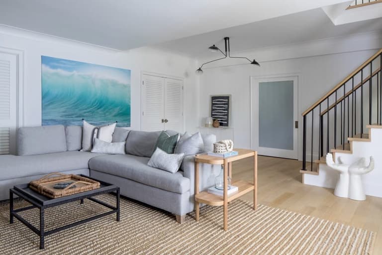 Living area of the Mroz family home in Westfield, NJ, with a gray sectional, a large wave painting and the stair rising behind
