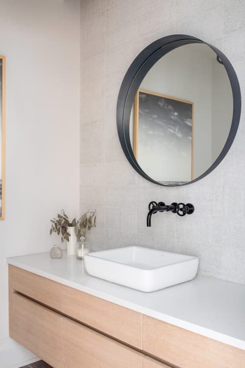 Vessel basin on a floating oak vanity with a matte black wall-mounted tap and a round mirror in a Westfield, NJ bathroom