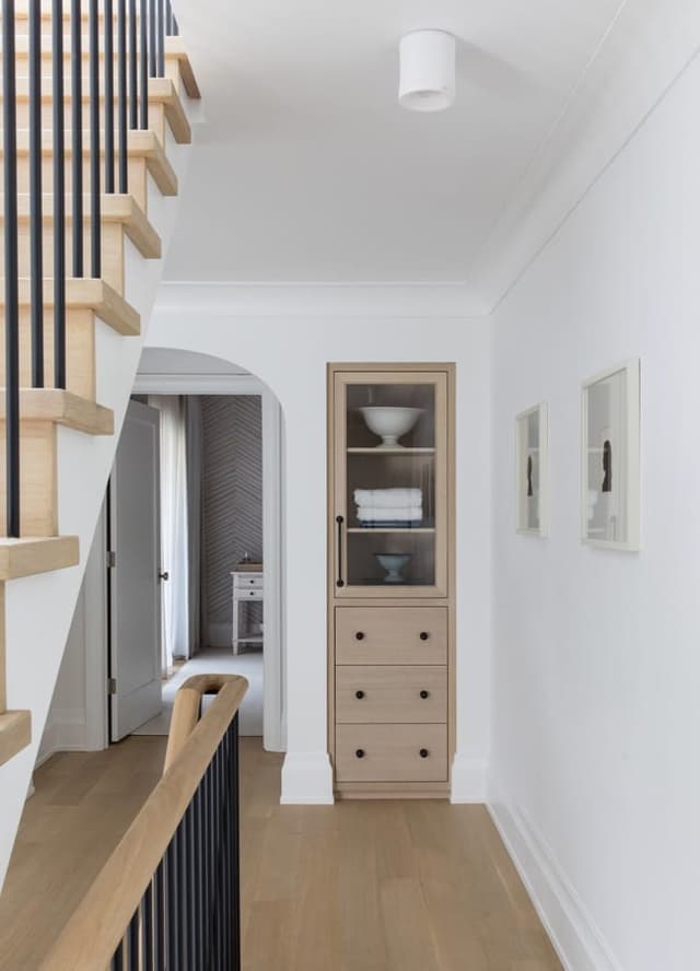 Stair of a Westfield, NJ home with open oak treads and black balusters, beside a narrow glass-front cabinet in the hall