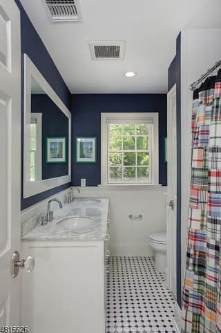 Children's bathroom in a Westfield, NJ coastal colonial renovation, with navy walls above white wainscot, a mosaic tile floor and a plaid shower curtain