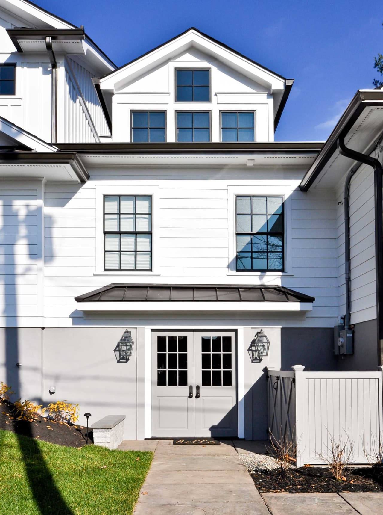 Side elevation of a white clapboard home with black windows, a standing-seam roof over the side entry and French doors in Westfield, NJ