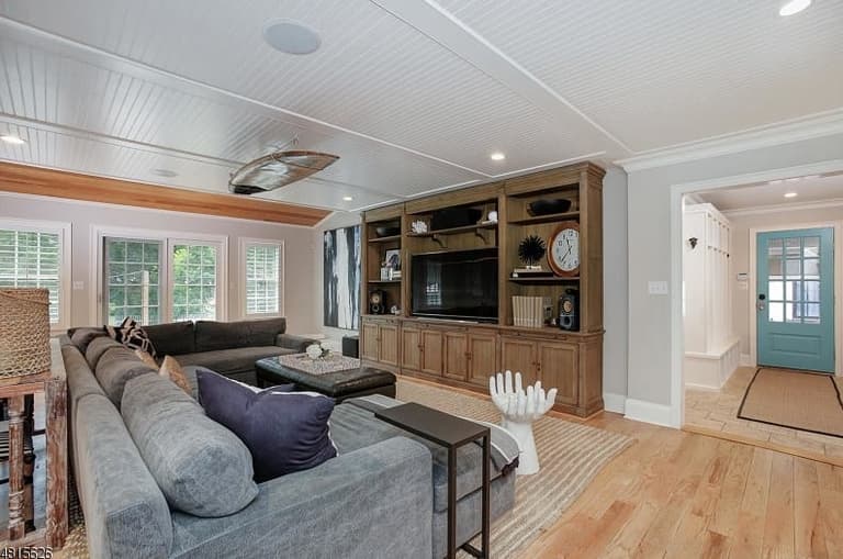 Family room of a Westfield, NJ coastal colonial renovation, with a beadboard ceiling, a wall of built-in cabinetry and a sectional on wide-plank floors