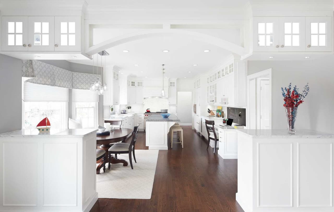 Kitchen and dining area under a barrel-vaulted ceiling, with white cabinetry and dark wood floors