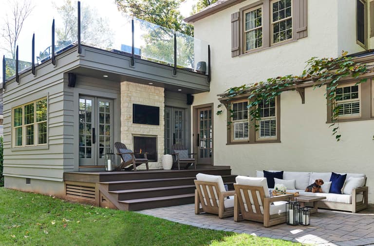 Back of a stucco and stone home with a flat-roofed addition, a roof deck above it and a vine-covered wall over the terrace seating