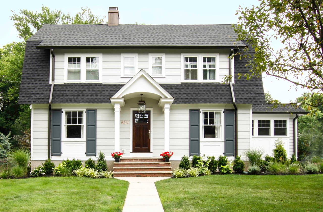 Front elevation of a white clapboard Dutch Colonial with a gambrel roof, dark gray shutters and an arched portico in Westfield, NJ